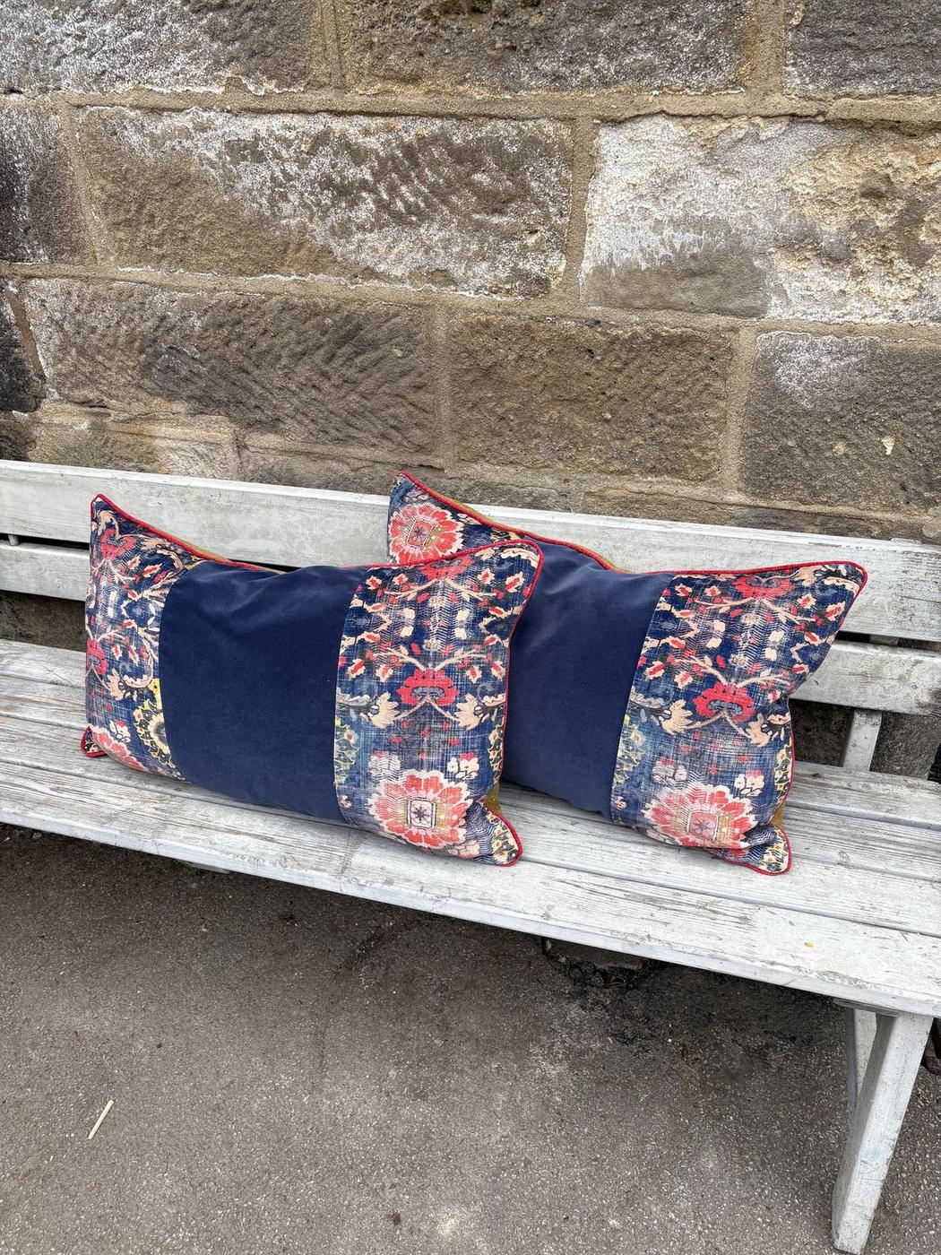 Floral and navy velvet bolster cushions on a garden bench