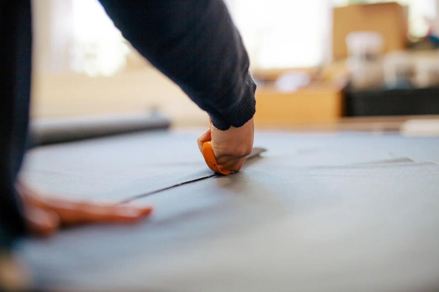 Hands marking a straight line across fabric before cutting
