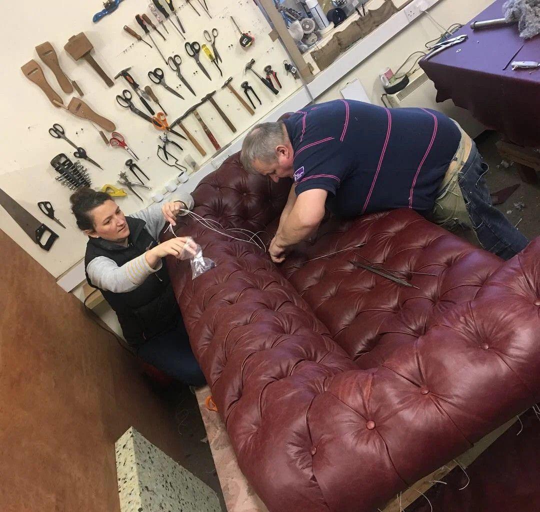 Two upholsterers buttoning a deep red leather chesterfield in the workshop