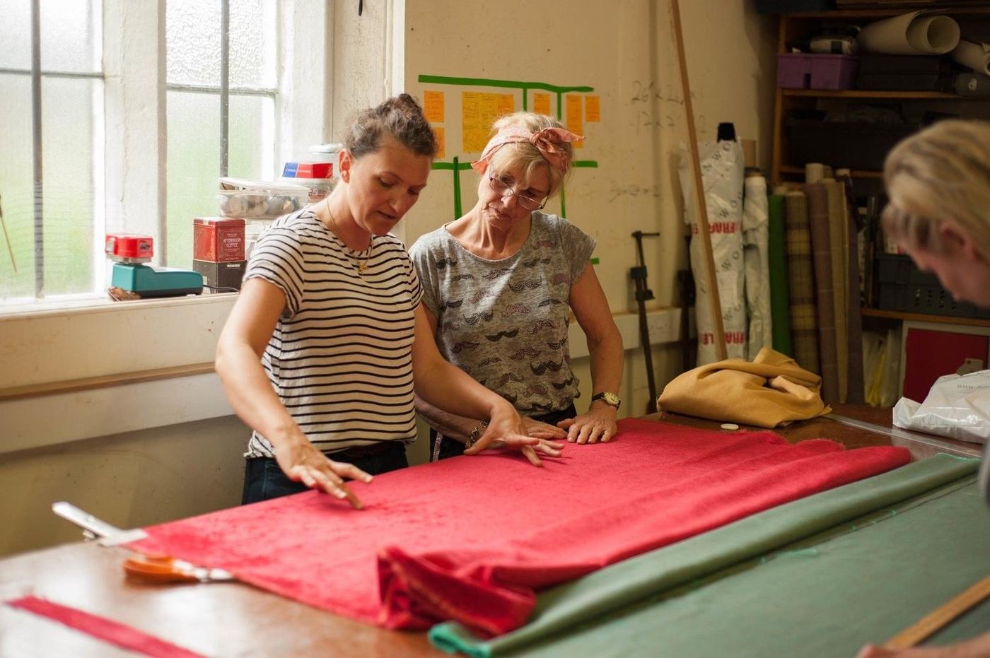 Two upholsterers marking out red fabric on the cutting table
