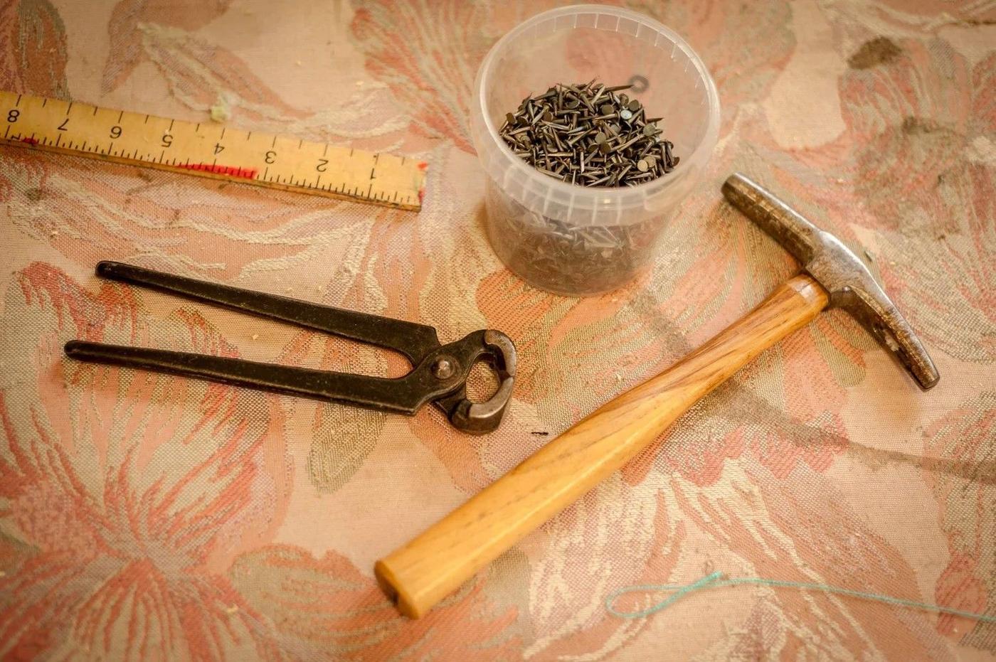 Upholstery tacks, a tack hammer and pincers on a workbench