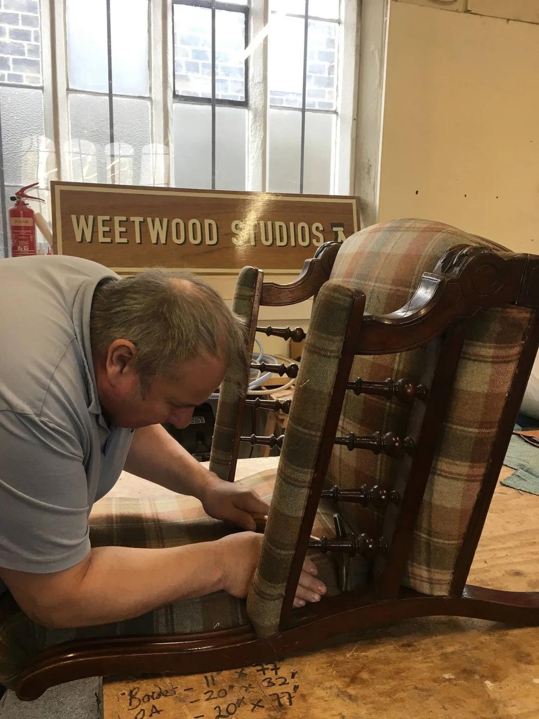 Stripping an old chair frame back in the workshop, Weetwood Studios sign behind